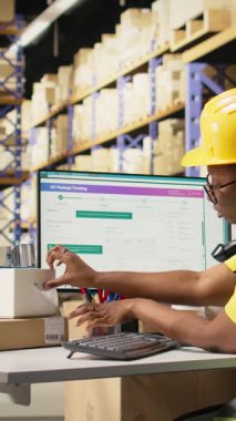 Dikey Video Siyah çalışanı barkodları uygulayıp tarıyor kargo kutularına etiketler yerleştiriyor, dağıtım öncesi malları ve sevkiyat detaylarını kaydediyor. Depodaki takip numaraları için tarayıcı kullanılıyor