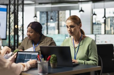 Çeşitli kadınlardan oluşan güçlendirilmiş ekip, verileri kavrayış ve vizyoner bir zihniyetle verimlilik ve takım çalışması sergileyerek kurumsal bir çalışma alanında dizüstü bilgisayar kullanıyor. Gelişim için mücadele.