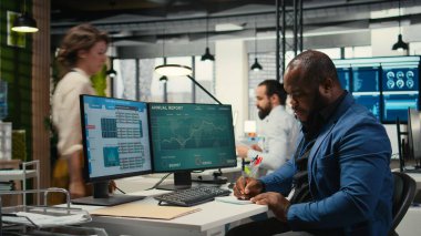 Siyahi çalışanlar notlarla yeni bir kalkınma stratejisi geliştiriyor, öngörü projesi sonuçlarına ilişkin verileri ve çözümleri analiz ediyorlar. Erkek profesyonel ofiste brifing raporları üzerinde çalışıyor..