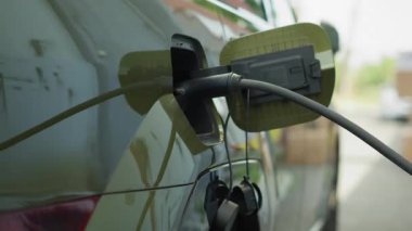 PEV elektrikli arabanın şarj cihazına bağlanması, sera gazı emisyonlarının azaltılması, çevre dostu ulaşım kavramı. İstasyonda EV otomobili şarj et, el kamerası görüntüsü