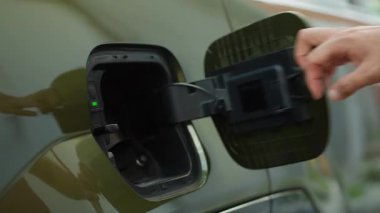 Sürücünün EV araç aküsünü şarj ederken yakın plan görüntüsü. Bir kişi yenilenebilir enerji kaynağına takılarak EV arabasının bataryasını şarj eder