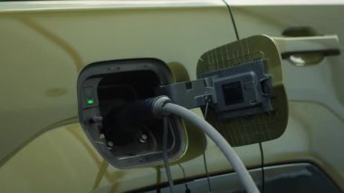 Yükleme limanına bağlı EV aracının kapatılması sürdürülebilirlik kararlılığını vurguluyor. Elektrikli arabanın güç kaynağına takılı görüntüsü, küresel çevre dostu taşımacılığın bir parçası.