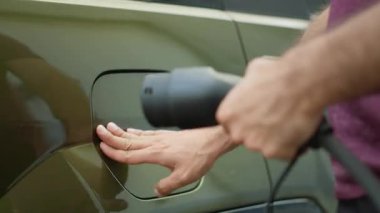 Eko-bilinçli sürücünün, yenilenebilir enerji taşımacılığına geçişi desteklemek amacıyla, şarj edilecek elektrikli arabanın iskele kapağını açmasını kapatın. Adam EV aracına elektrik kablosu bağlıyor