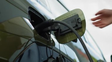 Sürücünün EV aracının şarj limanından bağlantısını kesmesi, düşük karbon ayak izi taahhüdü kavramı. Elektrikli arabanın fişini çeken adam şarj üstüne şarj, düşük açılı çekim.