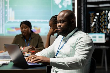 Afrika kökenli Amerikalı erkek analist, bütçe rakamlarını ve kaynak tahsisini gözden geçirip ekibiyle gece vakti yaptığı toplantıda dizüstü bilgisayardaki verileri inceliyor. Saatler sonra gece sahnesi.