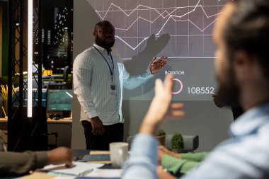 Genel müdür, ofisteki çalışanlarla birlikte yeni bir genişleme stratejisi hakkında bilgi paylaşımı yaparak, iş faaliyetlerini analiz etmek için veri raporları sunuyor. Toplantıda iş arkadaşları..