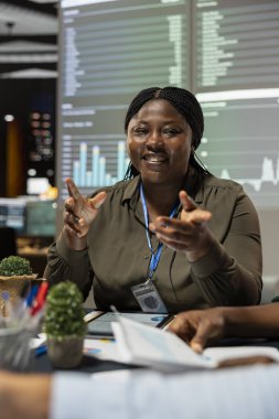 Gülümseyen siyah yönetici ekibiyle bütçe görüşmeleri yapıyor, veri tahminlerini değerlendirmek ve kaynak tahsisini yönetmek için toplanıyor. Kadın takım lideri ortakları topluyor..