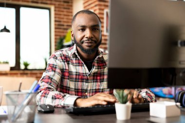 Odaklanmış Afro-Amerikan girişimci masaüstü bilgisayarında çalışıyor, pazarlama verilerini gözden geçiriyor ve son teslim tarihinden önce şirketin mali raporlarını güncelliyor. Ciddi, hedef odaklı uzaktan çalışan.