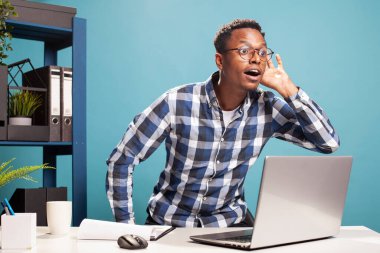 Erkek yönetici sandalyesinden kalkıp, ağzı açık ve eli kulağına kadar açık, bir şeyler duymaya çalışıyor. Meraklı adam masasından öne eğiliyor, açıkça duymak istiyor, dedikodularla ilgileniyor..