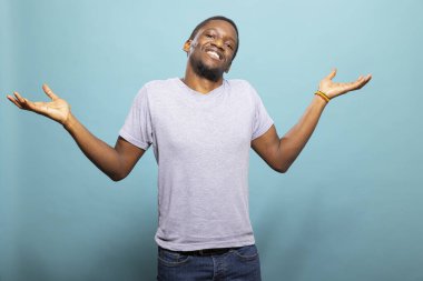 Afrika kökenli Amerikalı bir adam belirsizliğini belirterek izole bir arka plan üzerinde omuz silkiyor. Genç siyah erkek günlük kıyafetler giyiyor ve kameraya açık kollarla bakıyor..