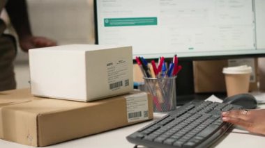 Kutuların sevkiyat detayları için barkodları tarayan Afrikalı Amerikalı bir kadın, paket izleme yazılımının hava yolu faturası verilerini doğru paket güncellemeleri ile kaydediyor. Tarayıcı teknisyeni. Kamera B.