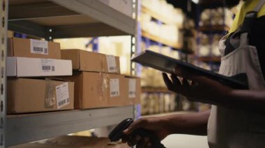 Endüstriyel raflardaki kargo etiketlerini işlemek için barkod tarayıcısı kullanan siyahi işçilere yaklaş. Paket izleme servisi için takip bilgileri ve lojistik bilgileri taranıyor. Kamera A.