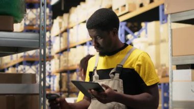 Siyah personel, raflardaki kutuların etiketlerini işlemek için barkod tarayıcısı kullanıyor. İz sürme bilgisi ve doğru lojistik ile paket izleme servisi için yanlış etiketler taranıyor. Kamera B.