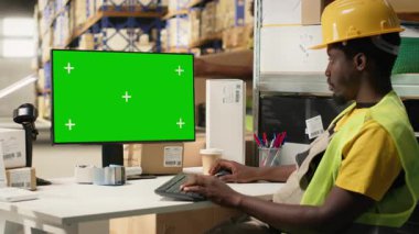 Zenci adam Chroma Key 'in yanındaki bilgisayarda yapılan e-ticaret operasyonlarını denetliyor, dağıtım merkezinde sevkiyat detaylarını hazırlıyor. Tedarik zinciri verimliliği yüksek yelek personeli tarafından destekleniyor. Kamera B.