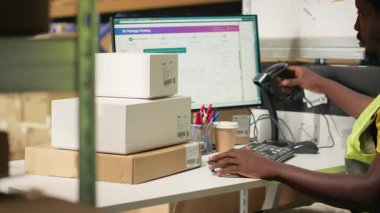 Afrikalı Amerikalı katip, büyük sanayi raflarındaki kutuların sevkiyat detaylarını kaydetmek için barkod tarayıcı kullanıyor. Paket izleme servisi için havayolu faturaları taranıyor, doğru lojistik. Kamera B.