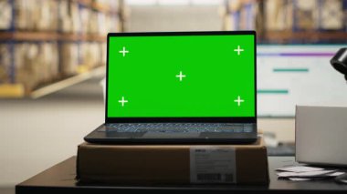 Modern depo tesislerinde dizüstü bilgisayarda yeşil ekran sergileniyor. Depo rafları ve raflarla çevrili çalışma masasında. E-ticaret ve düzenin sağlanması için büyük boş perakende ticaret.
