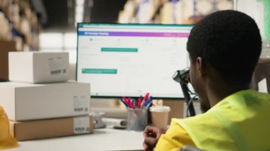 Afro-Amerikan tekerlekli sandalye kullanıcısı dağıtım merkezinde paket izleme bilgileri üzerinde çalışıyor, e-ticaret faaliyetleri için hızlı teslimat yönetmek için awb sevkiyat detaylarını kullanıyor. Engelli dostu. Kamera B.