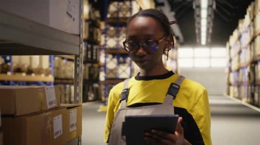 Lojistik merkezi kadın çalışanı envanter kaydı için havayolu faturalarını tarıyor, tabletteki ithalat ihracat sistemindeki kayıtları güncelliyor. Endüstriyel depoda e-ticaret operasyonları. Kamera A.