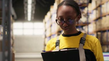 Afro-Amerikalı kadın, lojistik sistem, dağıtım merkezi, raflar ve nakliye protokolleri için ticari verileri inceliyor. Perakende satış ve tedarik zinciri. Kamera B.