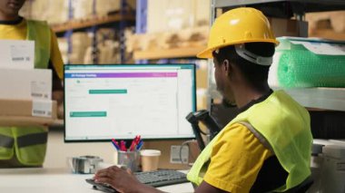 Siyah personel, endüstriyel depolama raflarındaki kargo etiketlerini işlemek için bir barkod tarayıcısı kullanıyor. Paket izleme servisi ve doğru lojistik bilgileri taranıyor. Kamera B.