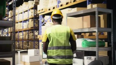 Siyah bir çalışan, endüstriyel depoda barkodları tarayıcı ile kaydediyor, dağıtım ve kargo sevkiyatıyla ilgileniyor. Çelik yelek ve çelik yelek ile çalışmak, yerine getirilmesi gereken siparişler. Kamera A.