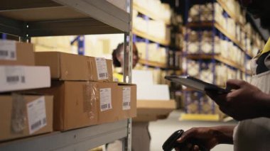 Afro-Amerikan e-ticaret çalışanları takip numaralarını tarıyor, nakliye etiketlerini ve depo envanter kayıtlarını kaydediyor. Paletler ithalat işlemleri ile ilgileniliyor. Kamera A.