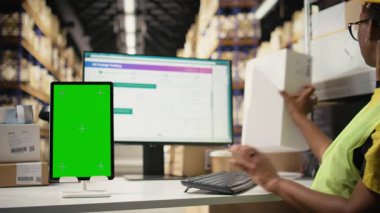 Sert şapkalı siyahi bir çalışan, depolama alanındaki sevkiyat detaylarını denetleyerek, modelleme ekranının yanındaki bilgileri takip ediyor. Yazılım üzerinden ekspres teslimat gözlemleniyor. Kamera A.