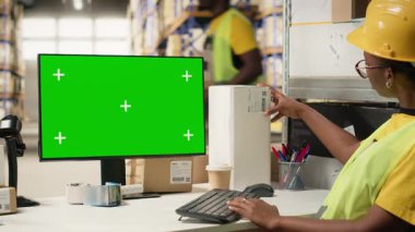 Kadın çalışan, fotokopi masasının yanındaki kutuların üzerindeki havayolu fatura etiketlerini onaylıyor. Dağıtım işlemleri için büyük askıları olan endüstriyel depoda yelek giyiyor. İnternetten alışveriş. Kamera B.