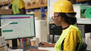 Barkodları ve sevkiyat detaylarını onaylayan siyah kadın etiketler ve izleme yazılımı, tedarik zinciri lojistiği ve e-ticaret dağıtımını yönetmeye odaklanıyor. İşçi envanteri gözden geçiriyor. Kamera B.