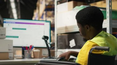 Özürlü Afrikalı Amerikalı erkek personel, yazılımın izlenmesi için havayolu fatura numaralarını kullanıyor, lojistik merkezindeki bilgisayardaki paket durumunu izliyor. Nakliye operasyonları. Kamera B.