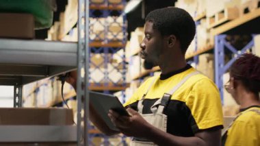 Afro-Amerikan e-ticaret işçisi nakliye etiketlerinin numaralarını tarıyor, envanter kayıtları ve sevkiyat detaylarını kaydediyor. Palet dağıtım operasyonlarıyla ilgilenen genç bir adam. Kamera B.