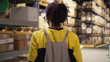 Afrika kökenli Amerikalı işçiler ticari lojistik sistemi için ürün işliyor, endüstriyel raflarla dolu bir depo alanı var. Çevrimiçi perakende satış merkezinde nakliye protokolleri. Kamera A.