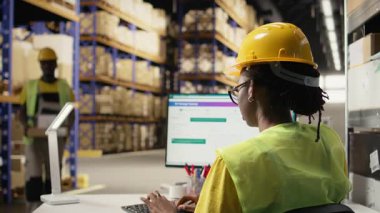 Yelek giyen Afro-Amerikan kadın barkodları tarıyor, paket sevkiyatı için, nakliye etiketlerinin takip edilmesini sağlıyor. Dağıtım için kargo bilgilerini onaylayan kasklı bir kadın. Kamera A.