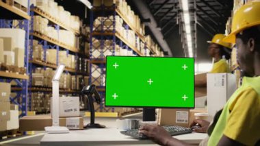 Zenci adam Chroma Key 'in yanındaki bilgisayarda yapılan e-ticaret operasyonlarını denetliyor, dağıtım merkezinde sevkiyat detaylarını hazırlıyor. Tedarik zinciri verimliliği yüksek yelek personeli tarafından destekleniyor. Kamera A.
