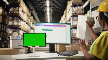 Afrika kökenli Amerikalı personel, bilgisayarında kroma anahtarı olan karton kutuları kontrol ediyor, paketin durumunu ve bilgisayar yazılımında havayolu fatura numaralarıyla sevkiyat rotasını izliyor. Yelekli kadın. Kamera A.