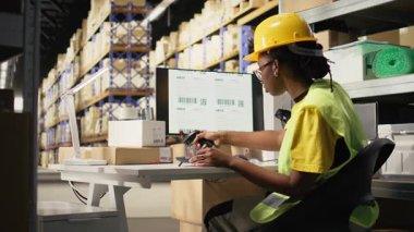 Yelekli siyah bir kadın tarayıcıyla takip bilgilerini kaydediyor, kargo siparişleri için ekspres teslimat servisini denetliyor. Etiketlerin sevkiyat detayları taranıyor, bilgisayar yazılımlarını takip ediliyor. Kamera A.