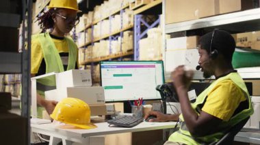 Afro-Amerikalı operatör müşterilere teslimat sorunlarında yardım ediyor, çağrı merkezinin yardım hattına büyük ölçekli e-ticaret deposunda cevap veriyor. Genç yetişkin çekleri gecikmeler, müşteri desteği. Kamera A.