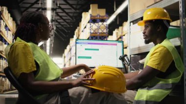 Siyah depo müdürü çalışanları için hayal kırıklığını ifade ediyor, sipariş gecikmelerini çözmek için paket izleme yazılımlarını kontrol ediyor. Dağıtım merkezinde baskı altında çalışan genç bir adam. Kamera A.