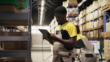 Afro-Amerikan e-ticaret işçisi nakliye etiketlerinin numaralarını tarıyor, envanter kayıtları ve sevkiyat detaylarını kaydediyor. Palet dağıtım operasyonlarıyla ilgilenen genç bir adam. Kamera A.