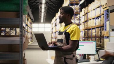 Depo görevlisi, büyük bir dağıtım merkezindeki rafların detaylarını inceliyor. Depoda güvenlik üniforması giyiyor. Malzeme zinciri yönetimi ve depolama odasına sevk. Kamera A.