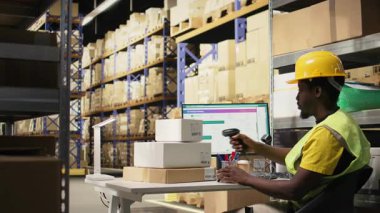 Afrikalı Amerikalı erkek çalışanlar büyük bir depoda paketleri tarıyor. Endüstriyel depo kayıtlarında havayolu faturalarını kaydediyor. Sipariş yerine getirmek için tarayıcı kullanılıyor. Kamera A.