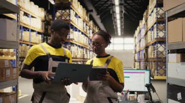 Afro-amerikan personeli envanter ve sevkiyat detaylarını kontrol ediyor. İş akışı ve verimli ticaret takibi için büyük ölçekli dağıtım işlemleri. Kamera A.