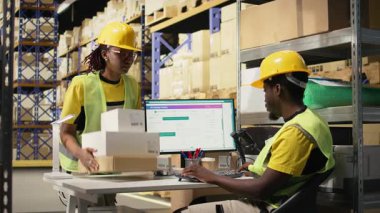 Siyah personel, endüstriyel depolama raflarındaki kargo etiketlerini işlemek için bir barkod tarayıcısı kullanıyor. Paket izleme servisi ve doğru lojistik bilgileri taranıyor. Kamera A.