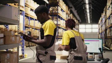 Teslimat merkezi çalışanı envantere kayıt olmak için nakliye etiketlerini tarıyor, tabletteki yönetim sistemindeki kayıtları güncelliyor. Sanayi bölgesinde e-ticaret perakende dağıtım operasyonları. Kamera A.