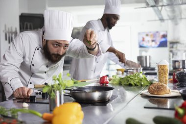 Bir restoranın mutfağında, şef ocakta taze kekik ve maydanozla bir tabak süslüyor. Genç aşçılık uzmanı renkli sebzeler ve baharatlarla, organik hammaddelerle yemek pişiriyor..
