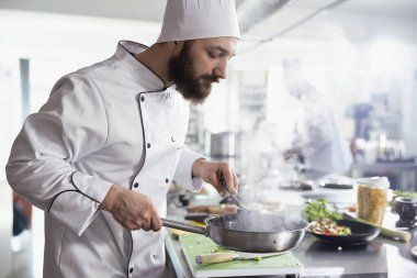 Erkek bir baş aşçı modern bir restoran mutfağında lezzetli bir yemek tarifi hazırlarken, tezgahta gurme tabağı üzerinde çalışırken buhar yükseliyor. Aşçılık sanatı tutkusu.