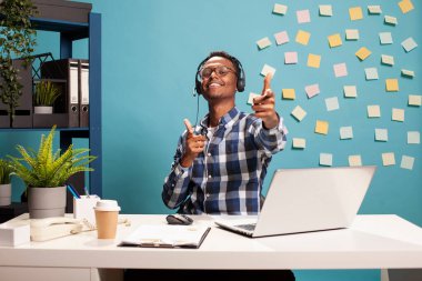 Kulaklıklı heyecanlı bir girişimci, kameraya bakıyor, projenin tamamlanmasından duyduğu memnuniyeti dile getiriyor. Siyahi yönetici ellerini öne uzatarak, başarılı iş görüşmelerini kutluyor..