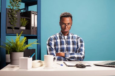 Genç ofis çalışanı kollarını kavuşturmuş, yavru köpek suratı yapıyor, masasında sevimli davranıyor. Gözlüklü siyah erkek analist, kameraya bakıyor ve aptalca bir ifade veriyor..