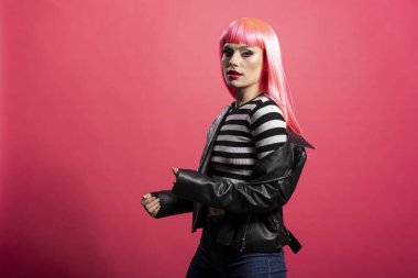 Çizgili bluzlu muhteşem bir kadın yumuşak ışığın altında kameraya bakıyor. Canlı saç stili ve parlak bir teni var. Siyah ceketli genç manken, pembe arka plana karşı durarak zarafetini sergiliyor.