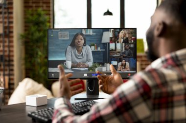 Siyah erkek girişimci, evden sanal toplantı sırasında başlangıç projesini sunuyor. Bilgisayarla masada oturan serbest çalışan bir adam, çok ırklı yatırımcılara iş fikirleri sunuyor..
